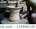 The skilled worker doing the clay work on the spinning wheel for modeling the shape of jar. 134406140
