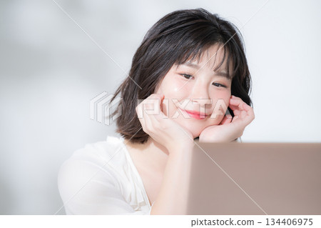 A young cute woman looking at a laptop. Relaxed, happy, fun. Spring pink image of qualifications, studying, etc. 134406975