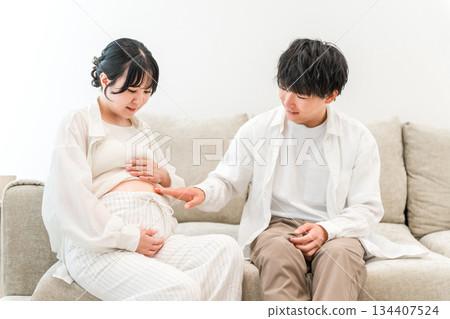 A man touching a pregnant woman's belly on the living room sofa in his home (family, dad) 134407524