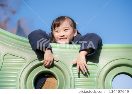 Children playing on playground equipment in a park under the blue sky. Image of children going out and having leisure time. 134407649
