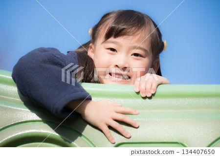 Children playing on playground equipment in a park under the blue sky. Image of children going out and having leisure time. Children playing on playground equipment in a park under the blue sky. Image of children going out and having leisure time. 134407650
