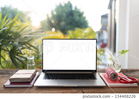 Laptop and gift box with craft paper wrap arranged on wood desk, with balcony view 134408226