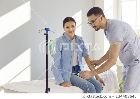 Young nurse or doctor help patient in receiving IV drip infusion and vitamin therapy in clinic 134408643