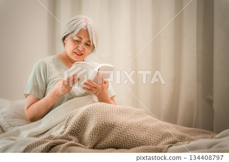 A gray-haired senior woman reading in her bedroom before going to sleep. A gray-haired senior woman reading in her bedroom before going to sleep. 134408797