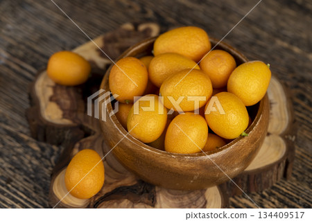 small orange fruits of juicy fresh and fragrant kumquat on a wooden table, oval oblong kumquat fruit scattered on a black table made of pine wood 134409517