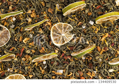 bright large dry lime slices and green tea with pieces of fruit, green tea with added flavors and pieces of fruit and cut dried green limes, closeup 134409530