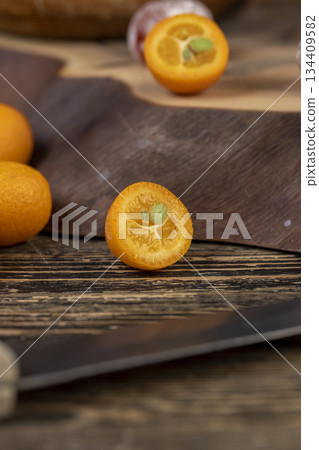 cut ripe orange kumquat cut in half on a wooden table, a group of scattered and sliced kumquat fruits on a wooden table and board cut ripe orange kumquat cut in half on a wooden table, a group of scattered and sliced kumquat fruits on a wooden table and board 134409582
