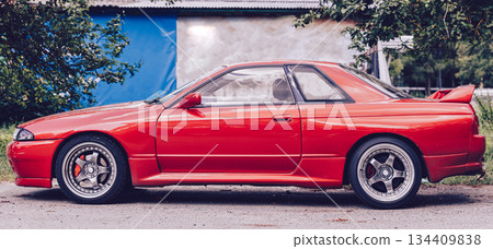 Panorama of the car. A bright red sports car, with a large rear spoiler and round taillights. A stylish retro feel and a strong emphasis on the car's design. Car racing, street racing. Panorama of the car. A bright red sports car, with a large rear spoiler and round taillights. A stylish retro feel and a strong emphasis on the car's design. Car racing, street racing. 134409838
