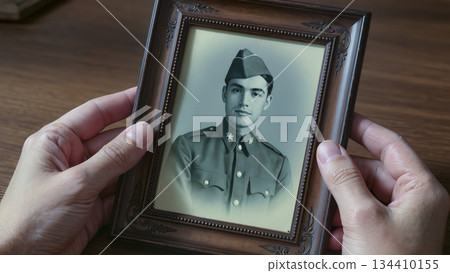 Hands holding an old black and white framed photo of a young soldier. Hands holding an old black and white framed photo of a young soldier. 134410155