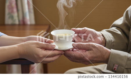 Caring for a Veteran: Hands Passing a Cup of Hot Tea to an Elderly Man 134410156