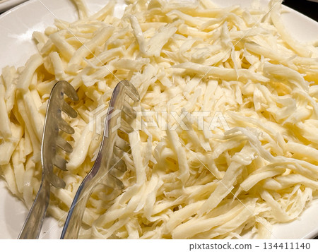 Grated white cheese served in large portion on buffet plate with tongs. Dairy ingredient preparation, cooking component, hotel breakfast catering, and self service food station. 134411140