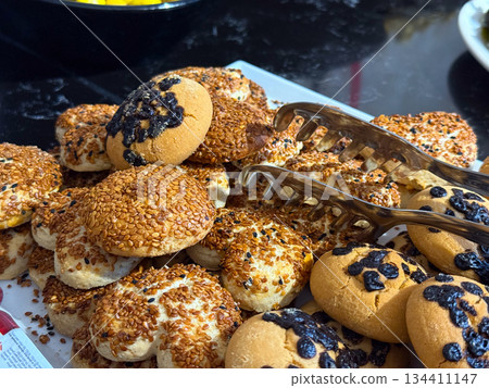 Assorted bread rolls and pastries with seeds arranged on serving tray. Bakery products, breakfast catering, carbohydrate foods, and fresh baked goods for hotel buffet. Assorted bread rolls and pastries with seeds arranged on serving tray. Bakery products, breakfast catering, carbohydrate foods, and fresh baked goods for hotel buffet. 134411147