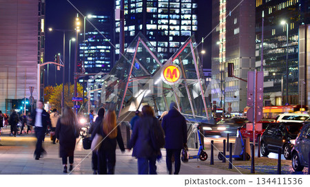 Warsaw, Poland. 4 November 2025. Entrance to the subway in center city in the night. People go to the subway. Lights street and buildings towering around them. Nearby with cars passing. 134411536