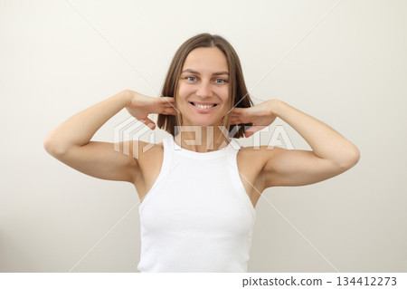 Happy young woman with flying hair smiling at camera on white backdrop. Casual natural look, raised arms, carefree emotion. Concept of freedom, fun, energy, youth branding, wellness, personal care 134412273