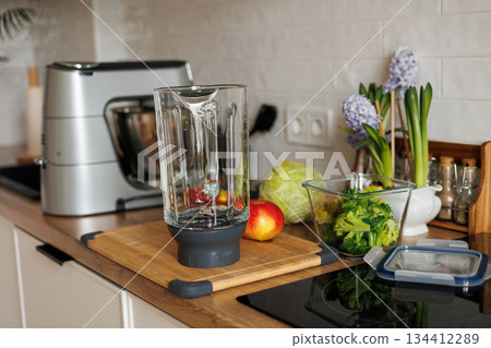 Healthy ingredients for detox smoothie drink and lifestyle diet. Glass blender bowl, apple, banana, broccoli, parsley on table top at modern home kitchen. Fresh fruits, vegetables and greens 134412289