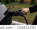 Unrecognisable woman inserting EV charger plug from public or home charging station for modern electric or hybrid car at special place for e-car. Concept eco-friendly sustainability energy car 134412291