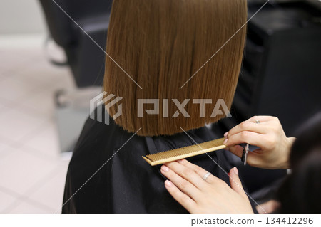 Unrecognisable hairdresser cutting female client hair with professional barber scissors and comb and making stylish haircut short bob hairstyle in beauty salon. Hair care, hair salon and hairstyling 134412296