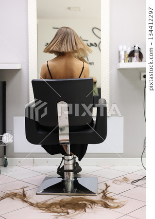 Rear view of woman with freshly right sleek bob haircut sits in chair, cut hair on floor in beauty salon. Clean lines and even length of the cut highlight. Concept of professional hairstylists work 134412297
