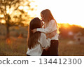 Family day, mother's day. Happy smiling young mom and adorable child daughter soft hugging, kissing and spending time together at autumn on sunset. Idyllic family having fun outdoors on fall holiday. 134412300