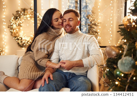 In love, sitting on the sofa. Couple is celebrating new year indoors together In love, sitting on the sofa. Couple is celebrating new year indoors together 134412451