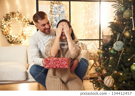Gift for a woman. Couple is celebrating new year indoors together Gift for a woman. Couple is celebrating new year indoors together 134412457
