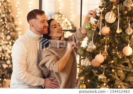 Side view, decorating the tree. Couple is celebrating new year indoors together 134412463