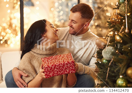 With red gift box, sharing love. Couple is celebrating new year indoors together With red gift box, sharing love. Couple is celebrating new year indoors together 134412470
