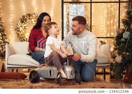 Kid is riding on the little bike. Happy family celebrating new year together at home 134412546