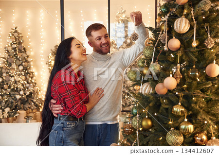Process of decorating Christmas tree. Couple is celebrating new year indoors together Process of decorating Christmas tree. Couple is celebrating new year indoors together 134412607
