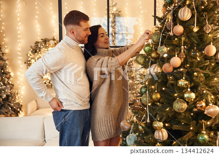 Decorating the Christmas tree. Couple is celebrating new year indoors together Decorating the Christmas tree. Couple is celebrating new year indoors together 134412624