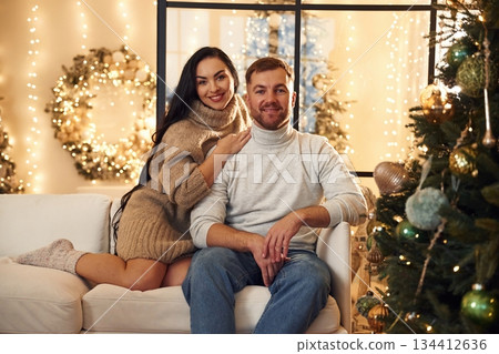 Sitting and smiling. Couple is celebrating new year indoors together Sitting and smiling. Couple is celebrating new year indoors together 134412636