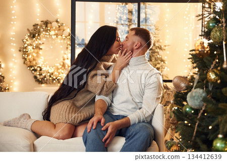 In love, sitting on the sofa. Couple is celebrating new year indoors together In love, sitting on the sofa. Couple is celebrating new year indoors together 134412639