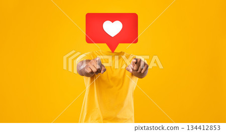 A person wearing a yellow shirt points toward the viewer in a vibrant setting filled with a bright yellow background. Instead their head is heart icon symbolizing likes and affection in social media. A person wearing a yellow shirt points toward the viewer in a vibrant setting filled with a bright yellow background. Instead their head is heart icon symbolizing likes and affection in social media. 134412853