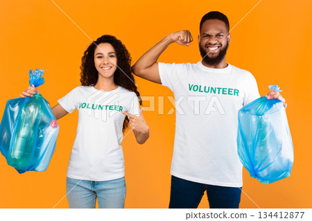 Volunteers Team. Multiracial Man And Woman Holding Blue Garbage Bags With Wasted Plastic Posing In Studio Over Yellow Background. Keep Environment Clean, Ecology And Volunteering Job Volunteers Team. Multiracial Man And Woman Holding Blue Garbage Bags With Wasted Plastic Posing In Studio Over Yellow Background. Keep Environment Clean, Ecology And Volunteering Job 134412877