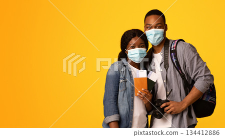 Coronavirus And Tourism. Portrait Of African American Couple In Medical Masks With Passports In Hands Ready For Vacation During Pandemic, Standing Isolated Over Yellow Studio Background, Copy Space Coronavirus And Tourism. Portrait Of African American Couple In Medical Masks With Passports In Hands Ready For Vacation During Pandemic, Standing Isolated Over Yellow Studio Background, Copy Space 134412886