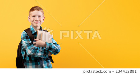 Cheerful schoolboy with backpack holding heap of books, yellow studio background, copy space. Happy boy going to school, holding books, enjoying his school days. Kids education concept Cheerful schoolboy with backpack holding heap of books, yellow studio background, copy space. Happy boy going to school, holding books, enjoying his school days. Kids education concept 134412891