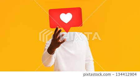 A person wearing a white long-sleeve shirt outstretching hand with large red heart icon instead of his head, bright yellow backdrop. This represents engagement on social media platforms. 134412904