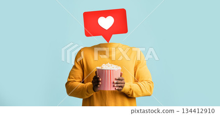 A person holds a bucket of popcorn while a heart icon appears above where their head should be. This visual represents social media interaction and engagement in a playful way. A person holds a bucket of popcorn while a heart icon appears above where their head should be. This visual represents social media interaction and engagement in a playful way. 134412910
