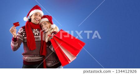 Christmas gifts. Romantic girl and her boyfriend with shopping bags and credit card on blue background, free space 134412926