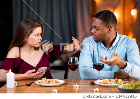 Annoyed Black Guy Blaming His Girlfriend For Using Smartphone During Romantic Dinner In Restaurant, Young Woman Showing Stop Gesture With Hand, Multicultural Couple Having Relationship Problems 134412930