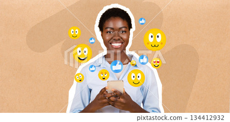 A young African American woman with a cheerful smile interacts with her smartphone, engaged in chatting and texting. Colorful social media emojis float around her, showcasing the digital communication 134412932