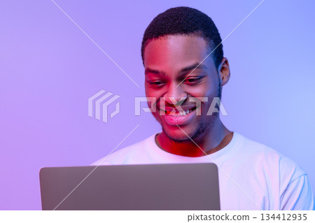 Handsome Smiling Black Programmer Guy Working Online On Laptop In Neon Light, Cheerful African American Freelancer Man Using Computer In Neon Light Over Purple Studio Background, Closeup Portrait Handsome Smiling Black Programmer Guy Working Online On Laptop In Neon Light, Cheerful African American Freelancer Man Using Computer In Neon Light Over Purple Studio Background, Closeup Portrait 134412935
