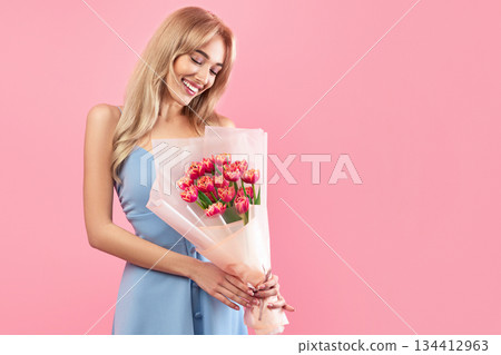 Positive young lady holding lovely tulips on pink studio background. Charming millennial blonde model with bunch of flowers for Woman's Day. Fun spring holiday concept Positive young lady holding lovely tulips on pink studio background. Charming millennial blonde model with bunch of flowers for Woman's Day. Fun spring holiday concept 134412963