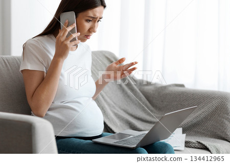Stressed Pregnant Woman Working Remotely With Laptop Computer And Talking On Cellphone At Home, Concerned Expectant Lady Suffering Business Problems, Sitting On Couch In Living Room, Copy Space 134412965