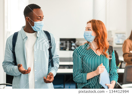 Youth, Lifestyle And People Concept. Group of diverse international students wearing protective medical masks and talking, black guy asking redhead woman on a date, standing in lecture hall Youth, Lifestyle And People Concept. Group of diverse international students wearing protective medical masks and talking, black guy asking redhead woman on a date, standing in lecture hall 134412994