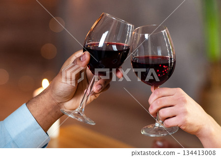 Happy interracial couple with glasses of red wine having date in restaurant, making toast for love. Affectionate multicultural lovers enjoying romantic dinner, celebrating valentine's day together Happy interracial couple with glasses of red wine having date in restaurant, making toast for love. Affectionate multicultural lovers enjoying romantic dinner, celebrating valentine's day together 134413008