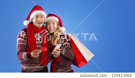 Romantic young couple shopping for Xmas gifts online with credit card and smartphone over blue background 134413068