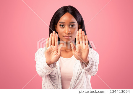 Millennial black woman gesturing STOP with both hands on pink studio background. Assertive African American lady saying NO, showing rejection gesture, expressing refusal or denial 134413094