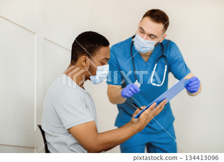 African American male patient signing papers before coronavirus vaccine injection at hospital. Black guy giving documented agreement to covid-19 immunization at clinic 134413096