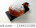 Round, delicious bun with cinnamon and powdered sugar on a black wooden board on a white background 134413108